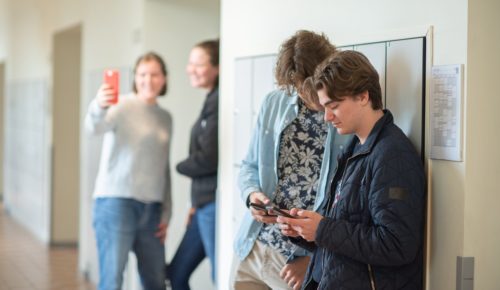 Äldre elever tittar på sina mobiler i en skolkorridor