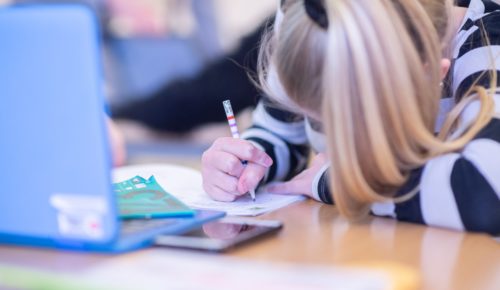 En flicka skriver i ett anteckningsblock framför en laptop