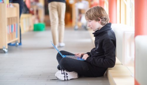 En pojke sitter i skolkorridor med en dator i knät.