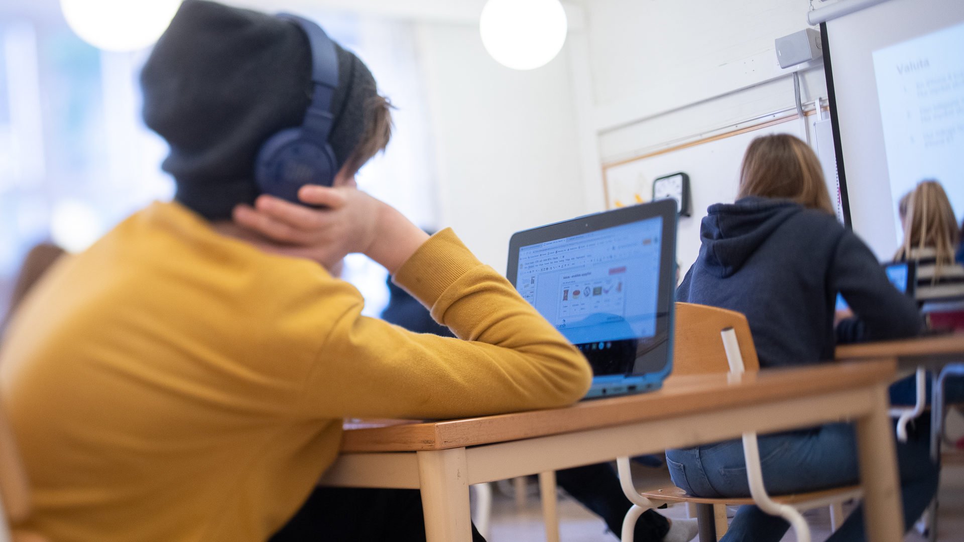 Elev sitter i förgrunden med hörlurar på och jobbar vid datorn.