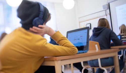 Elev sitter i förgrunden med hörlurar på och jobbar vid datorn.