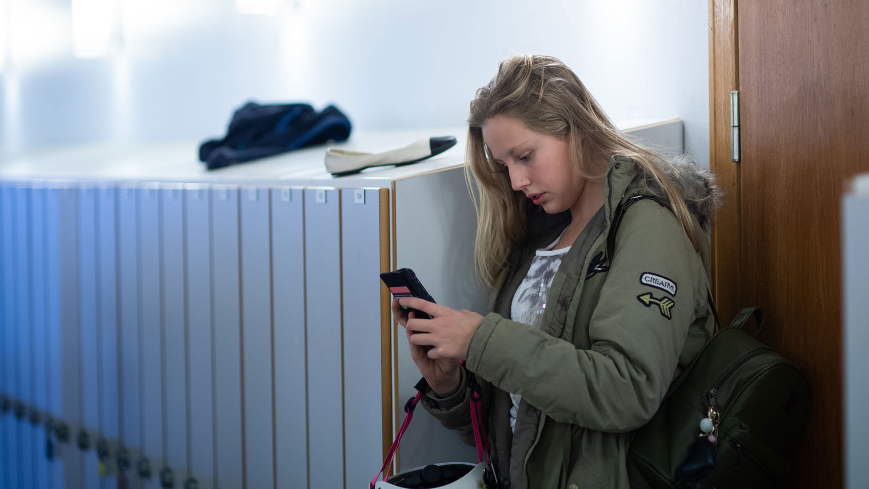 Ung tjej står i en korridor med sin smartphone i handen.