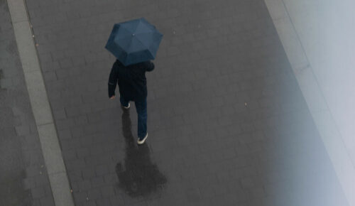 En person syns ovanifrån, hen håller i ett paraply och det är blött på marken.