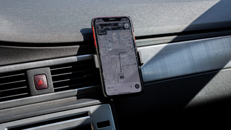 En telefon sitter fast på en instrumentbräda i en bil, på skärmen syns gps.