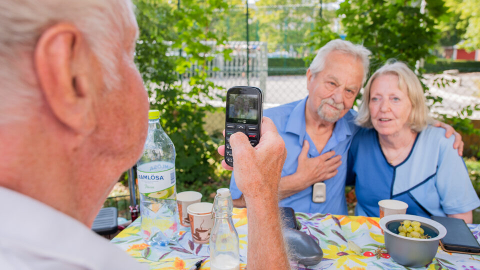 Ett äldre par blir fotade av en man som håller i en mobilkamera.