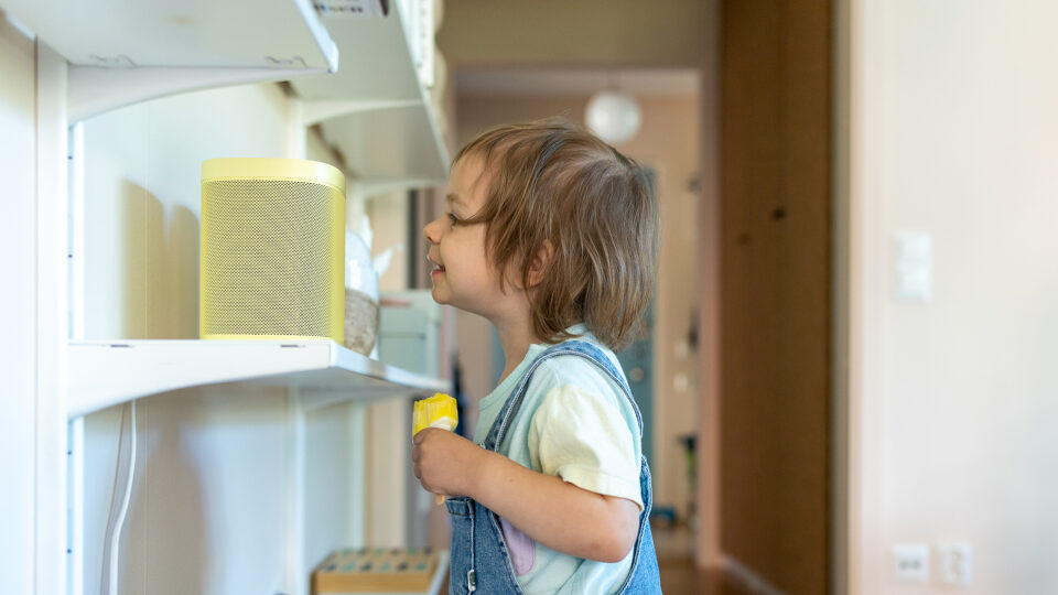 Ett barn står vid en högtalare med en glass i handen.