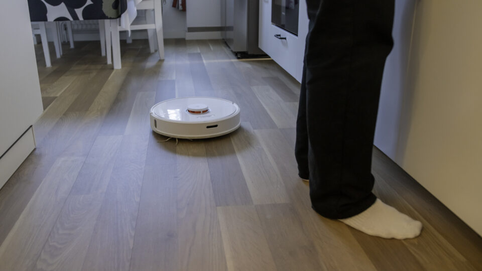Ett par fötter i ett kök, bredvid åker en robotdammsugare.