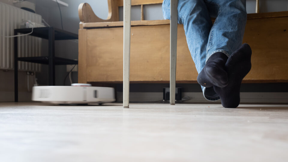 En kökssoffa med en persons fötter på golvet tillsammans med en robotdammsugare.
