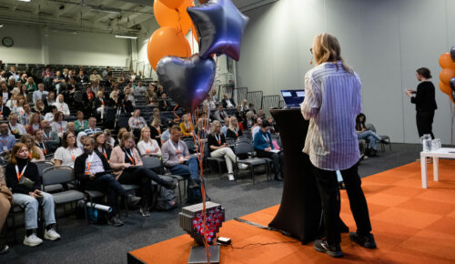 En person står på en scen framför en publik, talaren har ryggen mot kameran.