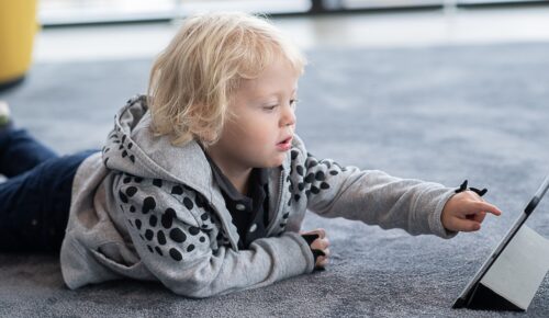 Ett barn ligger på mage på golvet och trycker på en ipad.