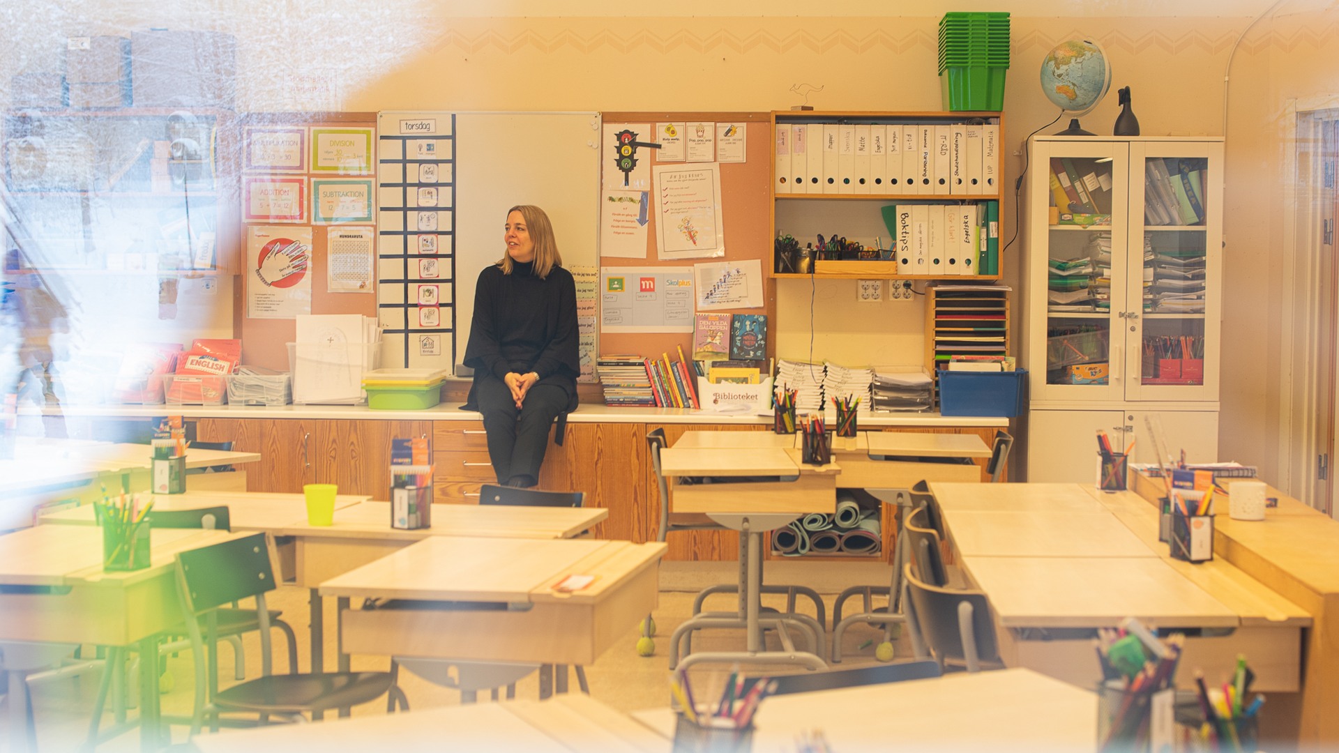 En lärare sitter på en bänk i ett klassrum.
