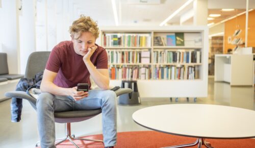 En man sitter i en stol och tittar på sin mobiltelefon