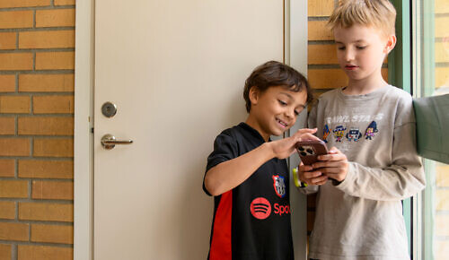 Två barn står i en skola och tittar på en mobiltelefon.