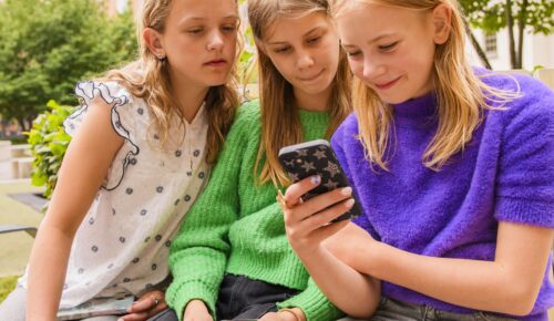 Tre tjejer sitter bredvid varandra och tittar på en mobil
